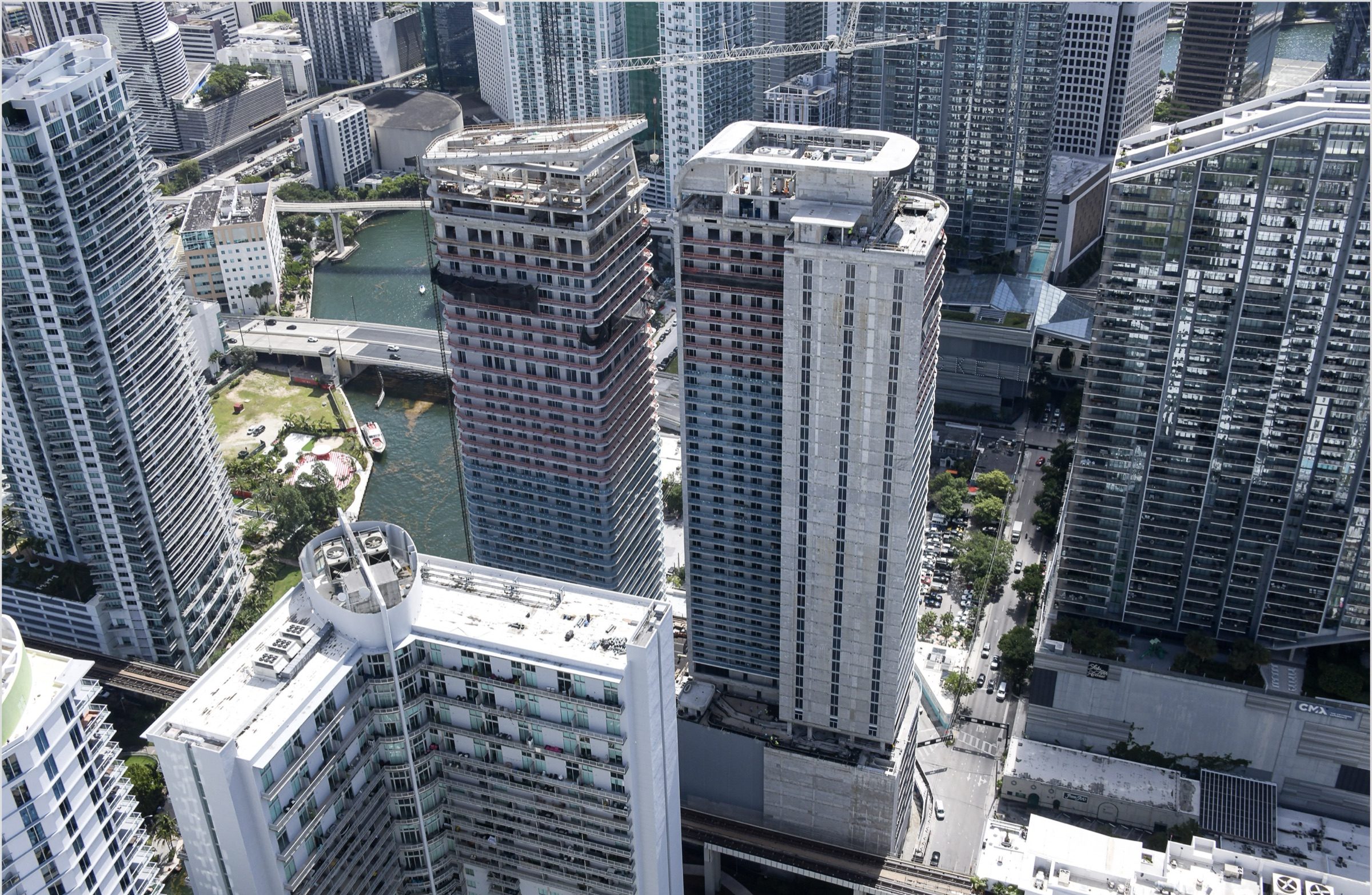 Construction aerial, May 2026: the riverfront and Brickell Key beyond